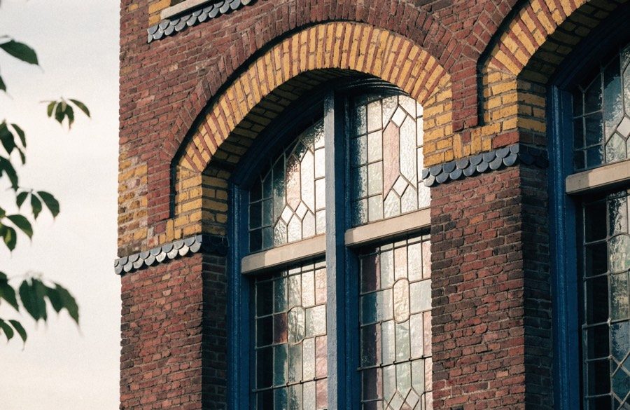Amsterdamse baksteengevel met gele siermetselwerkboog, geglazuurde tegellijst en oorspronkelijk glas-in-lood